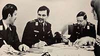 Die Redaktion 1979 Auf dem Schwarz-Weiß-Bild sitzen Soldaten mit Papier und Stiften an einem großen Tisch und reden miteinander.