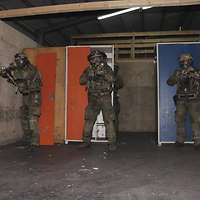 Drei Soldaten stehen mit Gewehr im Anschlag in einem Raum. Sie tragen Helme und ABC-Schutzmasken.