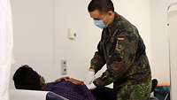 Ein Arzt in Uniform untersucht einen Patienten, beide tragen Mundschutz 