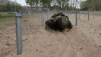 Ein Soldat mit Handschuhen, Helm und persönlicher Ausrüstung gleitet unter Drähten durch den Sand.