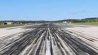 Auch Flugzeuge hinterlassen „Fußspuren“ Blick auf die Start- und Landebahn, die mit vielen schwarzen Spuren vom Gummiabrieb übersät ist.