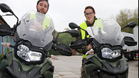 Ein Soldat und eine Soldatin sitzen mit Warnwesten auf Motorrädern und schauen in die Kamera.