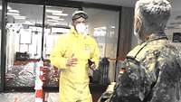 Ein Soldat in Vollschutz erklärt Generalstabsarzt Dr. Schmidt am Eingang zur Schleuse die Lage vor Ort.