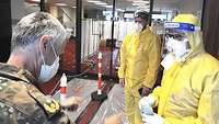 Zwei Soldaten in Vollschutz informieren Generalstabsarzt Dr. Schmidt über die Hygienevorschriften.