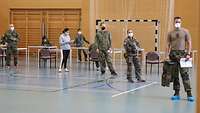 Fünf Soldaten und eine Soldatin im Sportanzug mit Maske warten in einer Schlange hintereinander.
