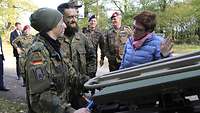Eine Soldatin und ein Soldat stehen an einem Fahrzeug und sprechen mit einer Zivilistin.