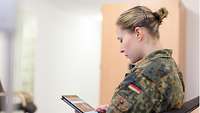 Eine Studierende in Uniform sitzt am Tablet und liest