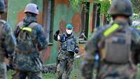 Ein Soldat wertet vor der Truppe den Übungsabschnitt aus, im Hintergrund ein Übungsgebäude.