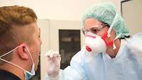 Eine Truppenärztin in Schutzkleidung entnimmt einem Patienten eine Rachenprobe mit Teststäbchen.