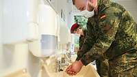 Zwei Soldaten mit Atemschutzmasken waschen sich in einem Hygienecontainer die Hände.