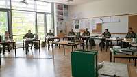 Fünf Soldaten sitzen nebeneinander in einem Unterrichtsraum, jeder an einem einzelnen Tisch.