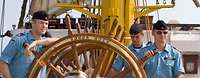 Gorch Fock Marine-Glossar Vier Marinesoldaten in blauer Arbeitsuniform halten ein großes, rundes hölzernes Schiffsruder.