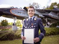 Die Verleihung des Ehrenkreuzes Ein Soldat steht mit einer Urkunde in der Hand vor einem Flugzeug.