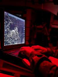 Ein Soldat sitzt in einem dunklen Raum vor einem Computermonitor 
