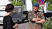 Zwei Personen stehen mit Abstand zueinander und unterhalten sich. Im Hintergrund ist eine Straße zu sehen.