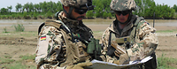 Ein Soldat mit Helm und Schutzbrille hält eine Karte, ein anderer zeigt etwas auf der Karte.