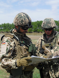 Ein Soldat mit Helm und Schutzbrille hält eine Karte, ein anderer zeigt etwas auf der Karte.