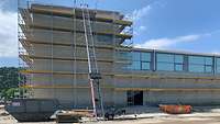 Außenfassade eines Gebäudes im Rohbau mit Schuttcontainer und Lastentransportleiter