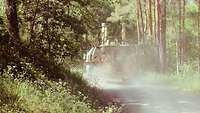 Panzer im Wald mit Staubwolke.
