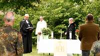 Drei Geistliche hinter einem Altar, einer von ihnen liest einen Urkundentext vor.
