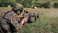 Ein Soldat liegt hinter dem Maschinengewehr, zielt und schießt. Patronen fliegen durch die Luft.