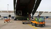 Ein Transportfahrzeug fährt an das geöffnete Heck der Antonov heran. Im dunklen Frachtraum sieht man die Container.