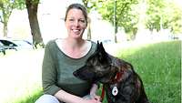 Eine Frau kniet neben einem Hund auf einer Wiese