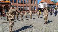 Einige Soldaten sind mit Abstand voneinander angetreten. Ein Soldat macht Meldung an den Kommandeur.