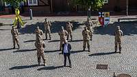 Luftaufnahme: Neun Soldaten in Wüstentarn und ein Zivilist stehen in Abständen auf einem Platz.