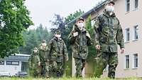 Mehre Soldaten mit Mundschutz gehen von links nach rechts