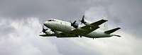 MPA P-3C Orion Ein hellgraues viermotoriges Propellerflugzeug im Flug vor grauem Himmel.