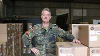 Soldat im Feldanzug steht in einem Lagerraum mit gepackten Kisten.