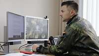 Ein Soldat sitzt in einem Büro. Vor ihm stehen zwei Bildschirme auf dem Schreibtisch.