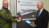 Zwei männliche Personen, eine davon in Uniform, präsentieren jeweils ein kleines Dienststellenwappen