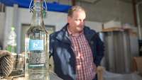 Im Vordergrund steht eine Flasche mit Trinkwasser, dahinter der Erfinder. Symbol für die Produkte der Firma.