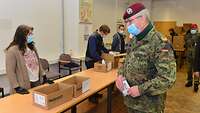Männliche Person in Uniform betrachtet zivile Personen, die auf Tischen vor ihnen Kartons packen