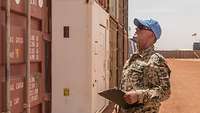 Ein Soldat steht vor einem Seecontainer und hält ein Klemmbrett in der Hand