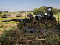 Soldaten der Bundeswehr üben im Gelände. Zwei Soldaten auf einem Waffenträger Wiesel im Gelände, im Hintergrund fahren zwei Panzer