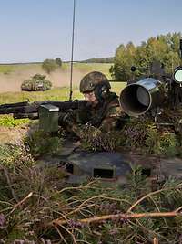 Soldaten der Bundeswehr üben im Gelände. Zwei Soldaten auf einem Waffenträger Wiesel im Gelände, im Hintergrund fahren zwei Panzer
