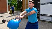 Mit einer Hantel trainiert eine Soldatin vor dem Sportcontainer ihren Rücken.