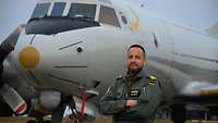 Ein Soldat in Fliegerkombi steht mit den Armenverschränkt vor einem Flugzeug