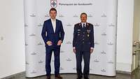 Ein Mann im Anzug und ein Soldat stehen nebeneinander zur Begrüßung. 