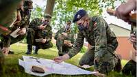 Rekruten in Uniform sammeln sich zur Ausbildung um eine Karte, die auf dem Boden ausgebreitet ist.