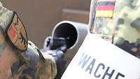 Ein Wachsoldat entlädt seine Pistole an der Waffenkiste, ein weiterer Wachsoldat überwacht die Tätigkeit.
