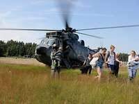 Bevölkerungsschutz bei Naturkatastrophen: Soldaten der Bundeswehr evakuieren Bürger Soldat hält ein Kind, mehrere Bürger laufen über ein Feld, im Hintergrund ein Hubschrauber am Boden