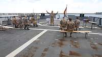 Ein Militärpfarrer predigt auf dem Flugdeck der deutschen UNIFIL-Korvette, mehrere Soldaten auf Bänken hören zu