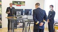 Drei Soldaten stehen mit Abstand in einem Raum. Einer davon redet mit jemandem, der per Videocall auf einem Monitor sichtbar ist