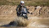 Stehend auf dem Motorrad durchfährt ein Kradmelder eine große Pfütze.