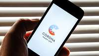 Corona-Warn-App Eine Hand hält ein Smartphone, auf dem das Logo der Corona-Warn-App der Bundesregierung angezeigt wird