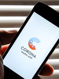 Eine Hand hält ein Smartphone, auf dem das Logo der Corona-Warn-App der Bundesregierung angezeigt wird